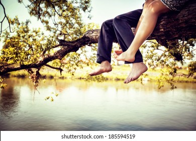 Young couple in love sitting cross-legged on a tree branch above the river in nice sunny day. Photo is colorized in warm tints. - Powered by Shutterstock