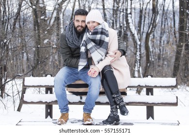 Young couple in love sitting on a bench in the snowy park