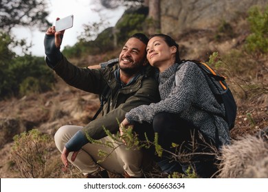 Young couple in love sitting on mountain trail and taking selfie. Happy young man and woman hiking in countryside and talking self portrait with mobile phone. - Powered by Shutterstock