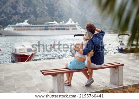 A young couple in love sitting on the bench in a hug and enjoying the view on the bay on a beautiful day. Love, relationship, holiday, sea