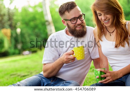 Young couple in love sitting on a picnic plaid in a park, drinking coffee and enjoying their day out in nature