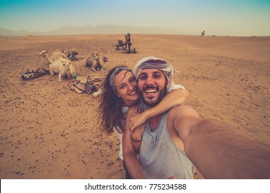 Young couple in love standing near many camels in africa desert taking photo with them, enjoying safari desert