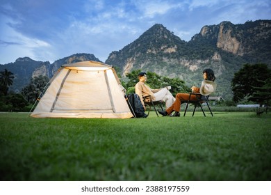 Young couple in love travelers sitting in chairs outside the tent drinking tea or coffee, resting talking during their time in the nature on vacation holiday with beautiful sunset background. - Powered by Shutterstock