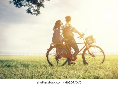 Young Couple In Love, Two Lover As Farmer With Bicycle In Love At Meadow With Vintage Sunset Lighting Photography.