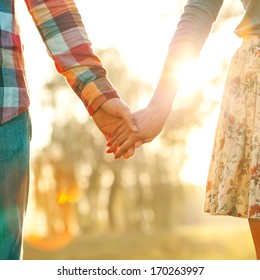 Young Couple In Love Walking In The Autumn Park Holding Hands Looking In The Sunset