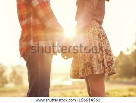 Young couple in love walking in the autumn park holding hands looking in the sunset