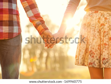 Young couple in love walking in the autumn park holding hands looking in the sunset