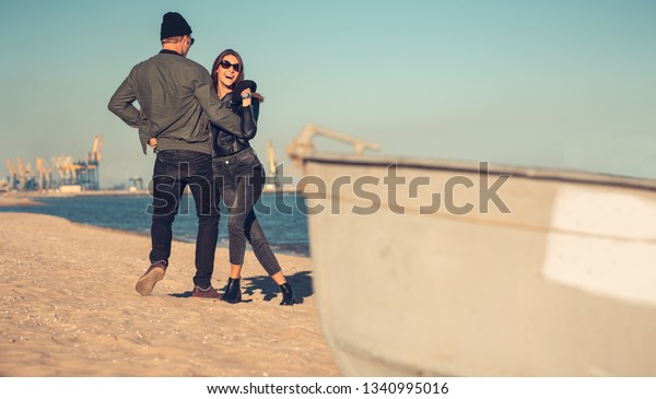 Young couple in love walks by the sea. Spring,\
autumn. The guy is wearing a jacket and hat. Girl in a hat and\
leather jacket with a\
scarf