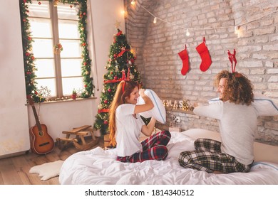 Young Couple In Love Wearing Pajamas, Having A Pillow Fight In Bed On Christmas Morning, Having Fun At Home During Winter Holiday Season