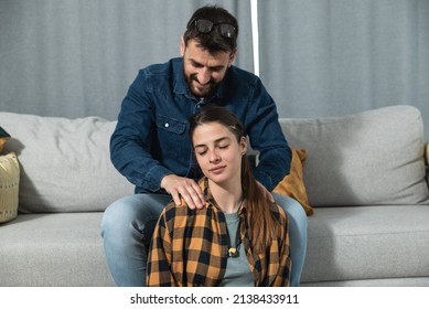 Young couple in love a woman sitting on the floor and a guy on the couch and gently massages her shoulders and head to relax her muscles after a hard day at work and to relieve her of stress.