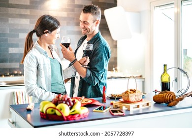 Young Couple Of Lovers Toasting Red Wine At House Kitchen - Happy Millenial People Enjoying Aperitif Time Cheering Together At Jubilee Anniversary - Genuine Youth Love Concept On Bright Natural Filter