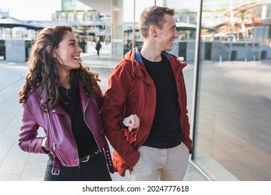 Young Couple Lovers Walking Around The City For Shopping, The Woman Smiles Looking At The Shop's Window, Concepts Of Love And Fashion Addicted