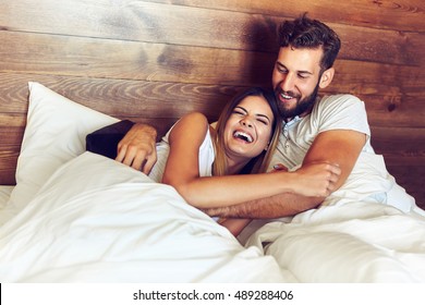 Young Couple Lying In Bed And Laughing While Tickling Each Other