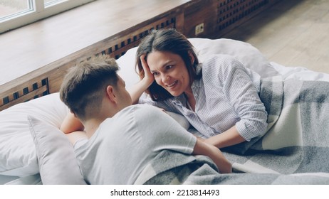 Young couple is lying in bed together and talking, pretty asian woman is speaking to her husband and laughing. Romantic relationship and family concept. - Powered by Shutterstock