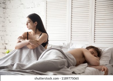 Young couple lying in bed under blanket at home. Boyfriend sleeping, pensive and frustrated girlfriend thinking about relationships break up or treason. Problem in sexual life concept