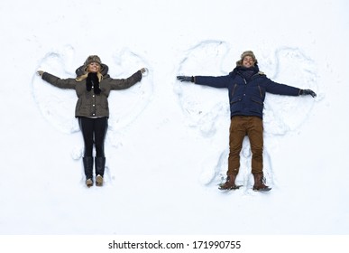 Young couple lying in fresh snow, making snow angels having fun.