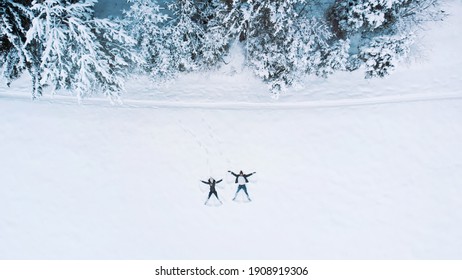 Young couple lying in fresh snow, making snow angels having fun near pine trees. Aerial. High quality photo - Powered by Shutterstock