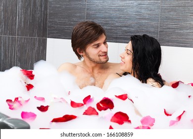 young couple lying in jacuzzi, tub full of foam and red rose petals, concept of romantic love