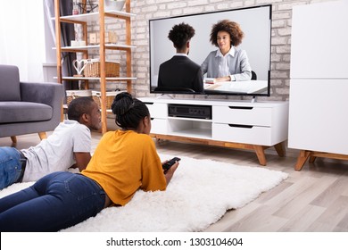 Young Couple Lying On Carpet Watching Television At Home