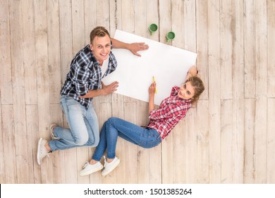 Young couple lying floor and cups drawing plan smiling joyful top view