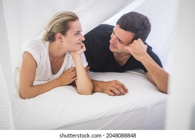 Young couple lying on front and staring at each other. Beautiful couple spending leisure with each other. Loving couple looking at each other on cozy bed at home