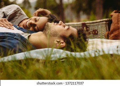 Young couple lying together on picnic blanket. Man and woman relaxing together at the park. - Powered by Shutterstock