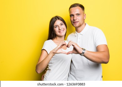 Young Couple Make Heart With Hands Isolated On Yellow Background