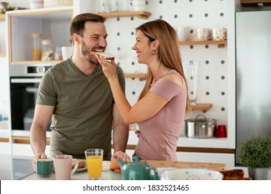 Young couple making breakfast at home. Loving couple eating sandwich in kitchen.