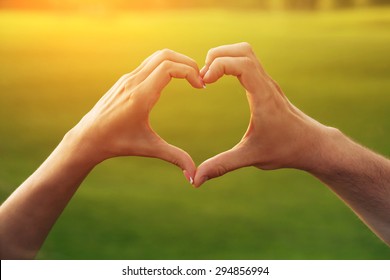 Young couple making heart. Female and male hands in the form of heart isolated on beautiful sunset.