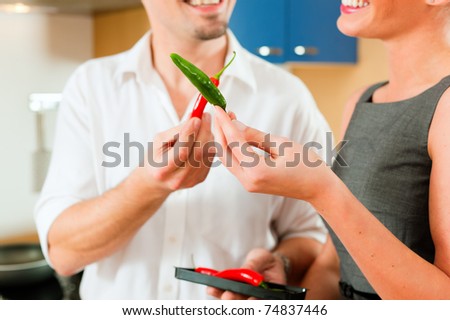 Young couple - man and woman - cooking in their kitchen at home, they having fun