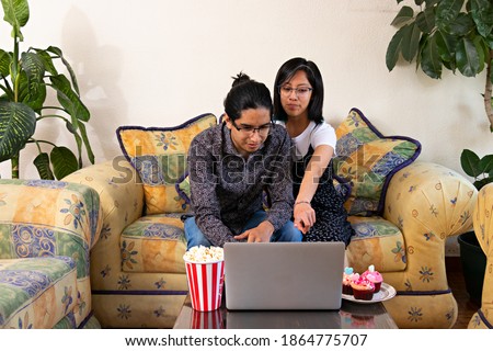Young couple of man and woman having a valentines day date, sitting in an armchair watching a movie on a computer