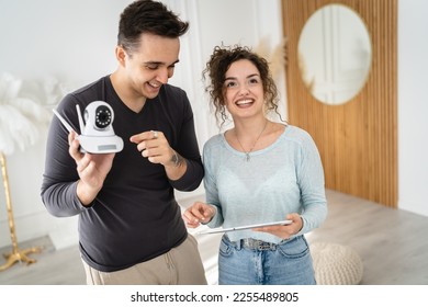 Young couple man and woman husband and wife or caucasian boyfriend and girlfriend setting up home surveillance security camera cctv protecting their home apartment bright room real people copy space - Shutterstock ID 2255489805