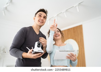 Young couple man and woman husband and wife or caucasian boyfriend and girlfriend setting up home surveillance security camera cctv protecting their home apartment bright room real people copy space - Shutterstock ID 2255489811