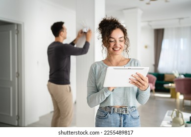 Young couple man and woman husband and wife or caucasian boyfriend and girlfriend setting up home surveillance security camera cctv protecting their home apartment bright room real people copy space - Shutterstock ID 2255489817