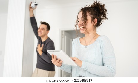 Young couple man and woman husband and wife or caucasian boyfriend and girlfriend setting up home surveillance security camera cctv protecting their home apartment bright room real people copy space - Shutterstock ID 2255489819