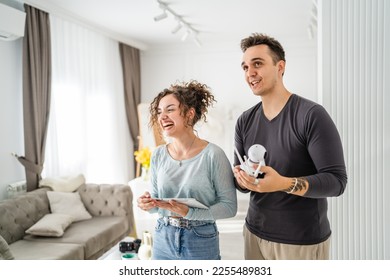 Young couple man and woman husband and wife or caucasian boyfriend and girlfriend setting up home surveillance security camera cctv protecting their home apartment bright room real people copy space - Shutterstock ID 2255489831