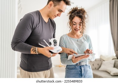 Young couple man and woman husband and wife or caucasian boyfriend and girlfriend setting up home surveillance security camera cctv protecting their home apartment bright room real people copy space - Shutterstock ID 2255489833