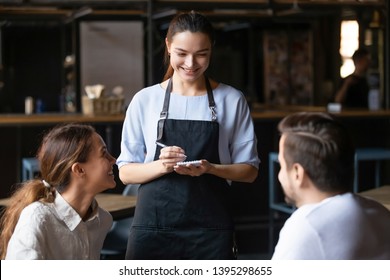 Young couple, man and woman ordering food in cafe, smiling waitress serving customers, attractive coffeehouse female worker talking with clients, consulting guests about menu, writing in notebook