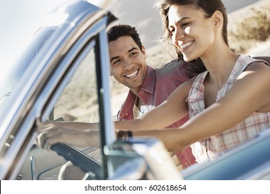 A Young Couple, Man And Woman In A Pale Blue Convertible On The Open Road