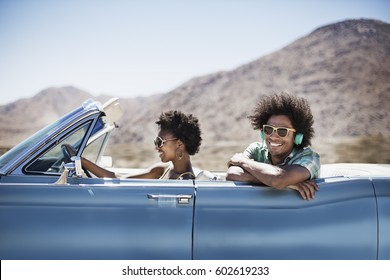 A young couple, man and woman in a pale blue convertible on the open road