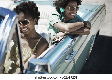 A Young Couple, Man And Woman In A Pale Blue Convertible On The Open Road