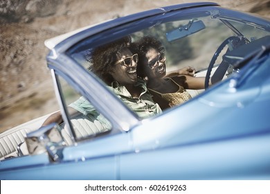 A Young Couple, Man And Woman In A Pale Blue Convertible On The Open Road