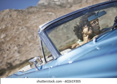 A Young Couple, Man And Woman In A Pale Blue Convertible On The Open Road