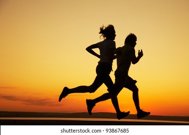 Young couple: man and  woman run together on a sunset on lake coast.  Silhouette. - Powered by Shutterstock