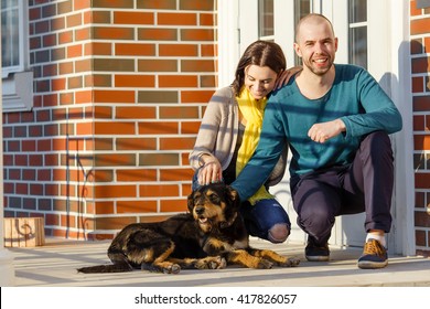 Young Couple Man And Woman Sitting With His Dog In Front Of The Door Of The House On The Porch Copy Space