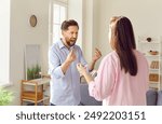 Young couple man and woman standing at home and arguing shouting in quarrel. Angry unhappy husband and wife quarreling in the living room. Marriage problems, relationship and divorce concept.