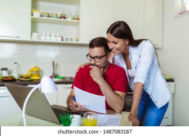Young couple managing finances, reviewing their bank accounts using laptop computer at modern kitchen. 