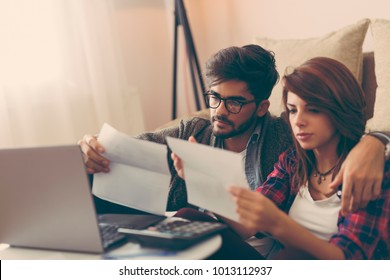 Young Couple Managing Their Finances, Reviewing Their Bank Accounts And Paying The Bills Using Laptop Computer. Focus On The Man