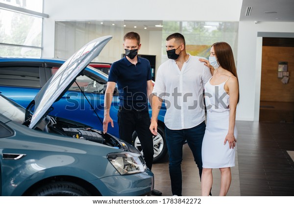 Young couple in masks\
selects a new vehicle and consult with a representative of the\
dealership in the period of the pandemic. Car sales, and life\
during the pandemic