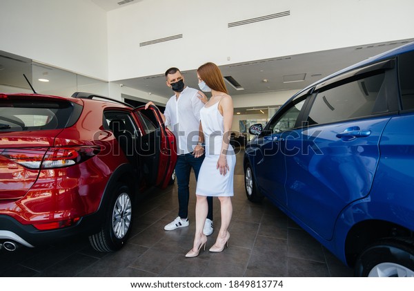 Young couple in masks\
selects a new vehicle and consult with a representative of the\
dealership in the period of the pandemic. Car sales, and life\
during the pandemic